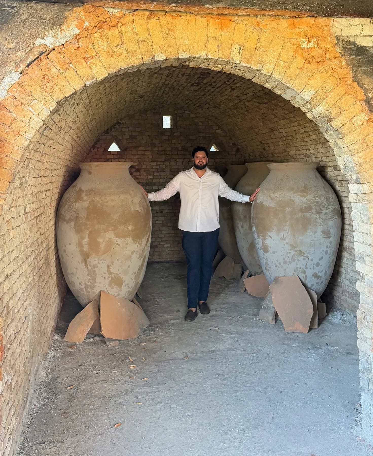 A person standing between two large clay qvevri vessels in a vaulted brick cellar
