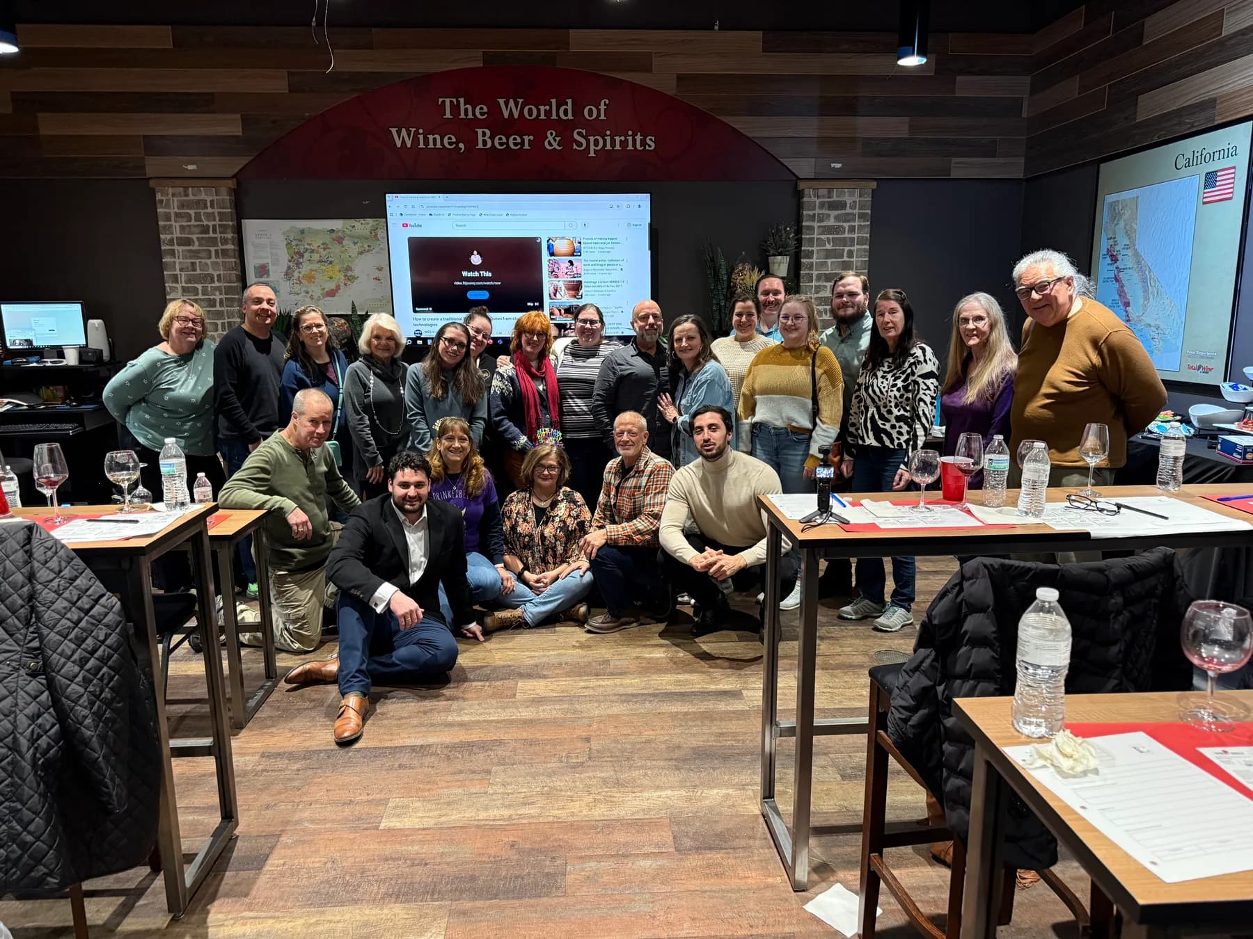 A large group gathered for a wine class in a Total Wine classroom, with glasses and tasting sheets on the tables