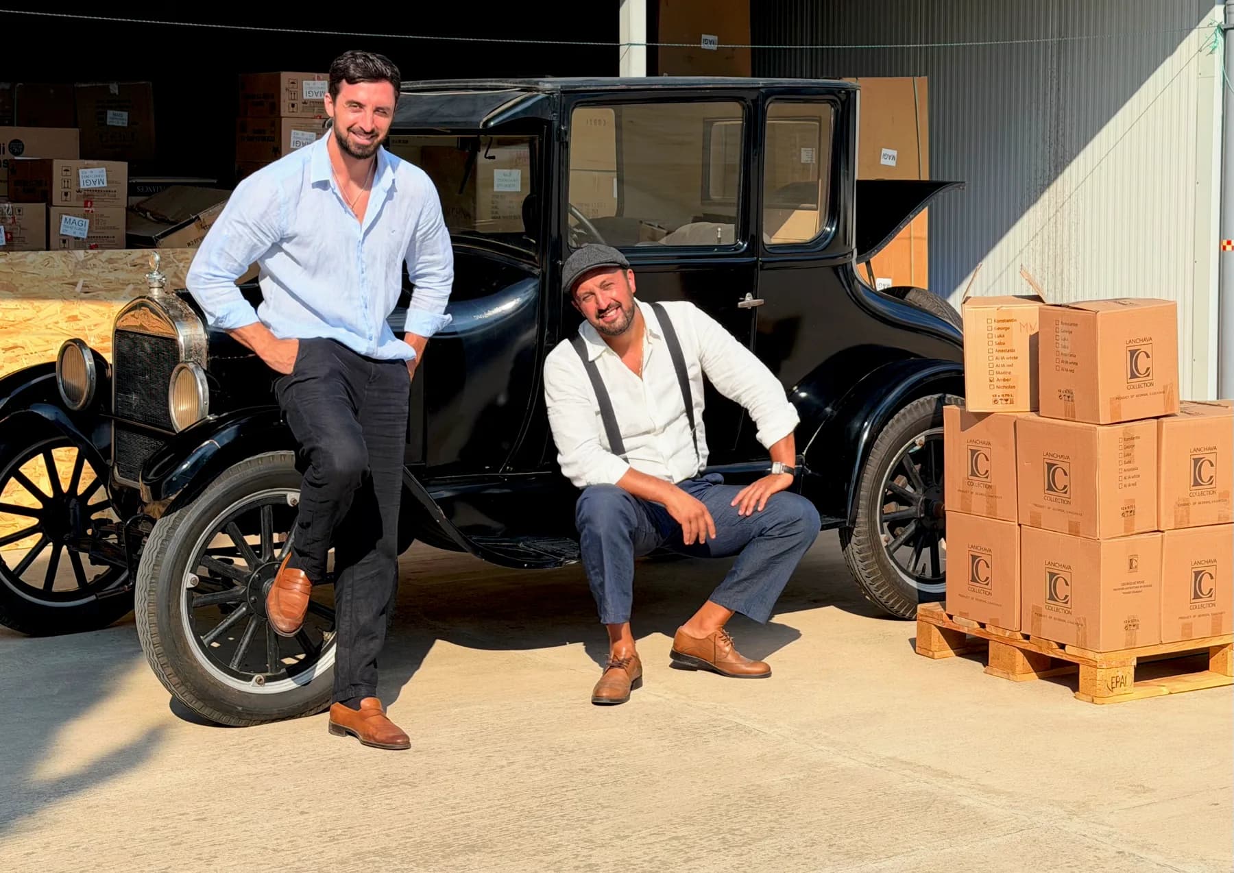 Two people in white shirts beside a vintage black car and a pallet of Lanchava Collection wine cases marked Product of Georgia